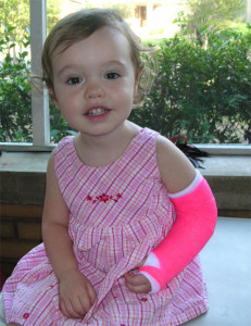 Little girl smiling with a broken arm in a pink cast