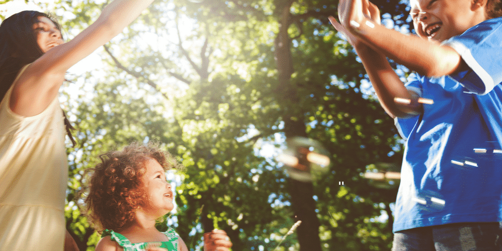 mom and little girl and older boy outdoors in trees and sun in blog post called Let Summer Be Time for Children To Play, Laugh, Learn and Heal