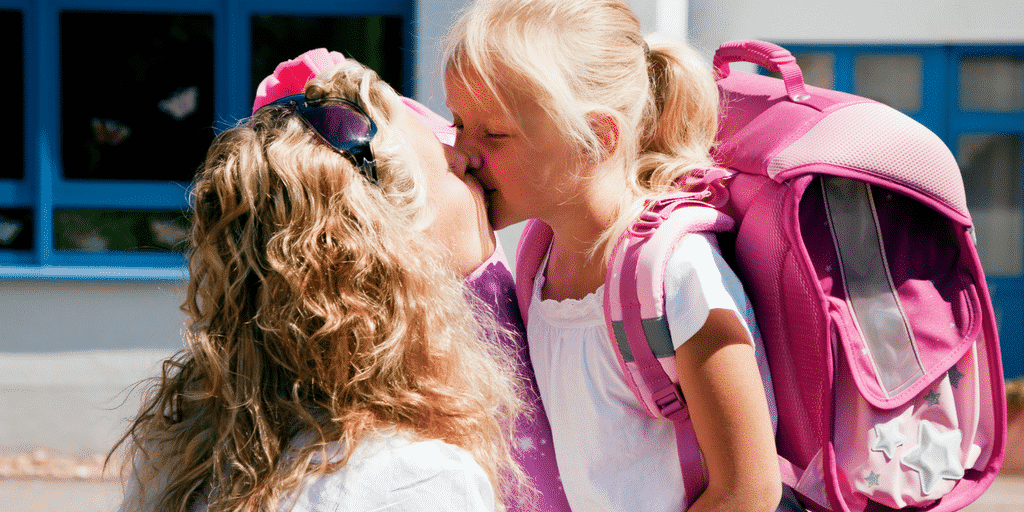 mum kissing happy girl on first day of school in post about emotional transitions