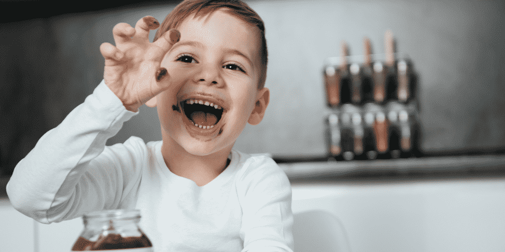 boy dipping his hand in jar of chocolate spread in post about connection parenting rewarding bad behavior