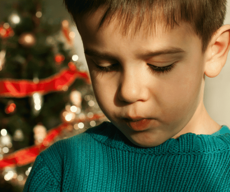 boy looking tearful in front of Christmas tree