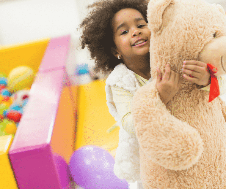 Little girl holds big teddy bear in post about how play helps teach manners