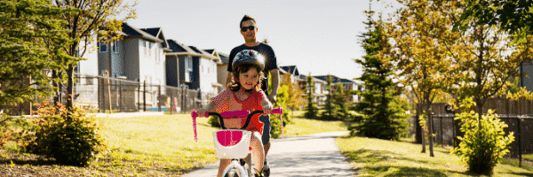 Girl builds resilience by facing her fear and riding her bike with dad in background
