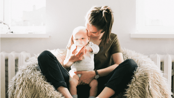 Tired mom holding baby in post about finding time for self-care by Rebecca Eanes


